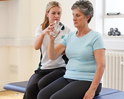 Elderly lady gets aid holding a glass of water by a trained ManchesterOT physio.